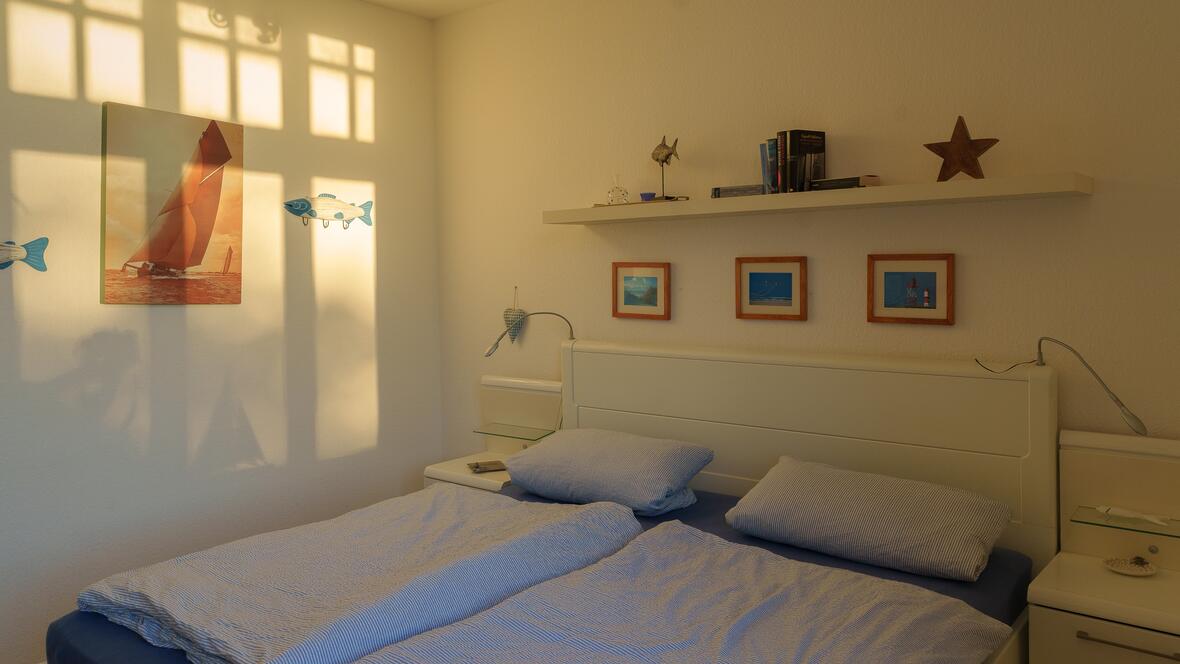 Das freundlich eingerichtete Schlafzimmer der Ferienwohnung Charlotte zeigt das Doppelbett, maritime Details und warmes Tageslicht - ideal für eine erholsame Unterkunft auf Borkum.
