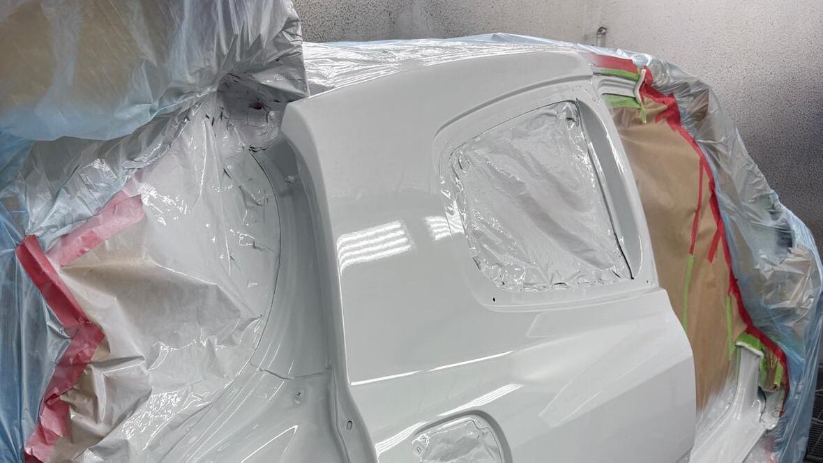 Weiß lackiertes hinteres Karosserieteil eines Autos in einer Lackierkabine, sorgfältig abgeklebt mit Folie und Papier für den Lackiervorgang.
